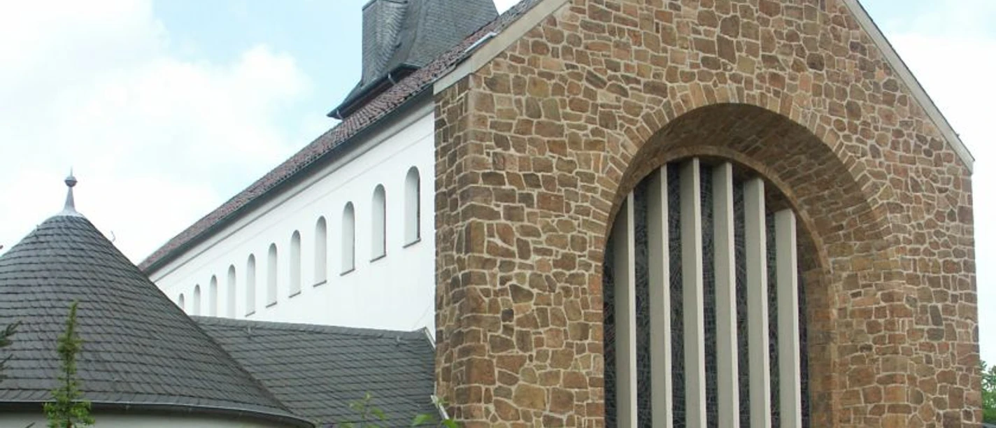 Steinverkleidete Fassade und schiefergedeckter Turm der katholischen Kirche St. Johannes Baptist.