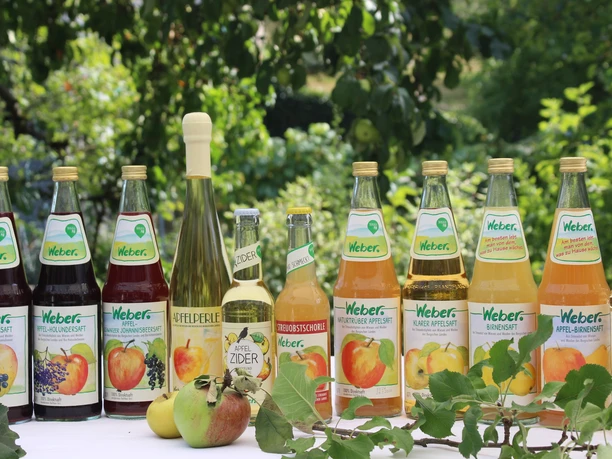 Weber Säfte Eine Auswahl an Weber Obstgetränken, darunter Säfte und Cider, ist auf einem Tisch in einem Garten ausgestellt.