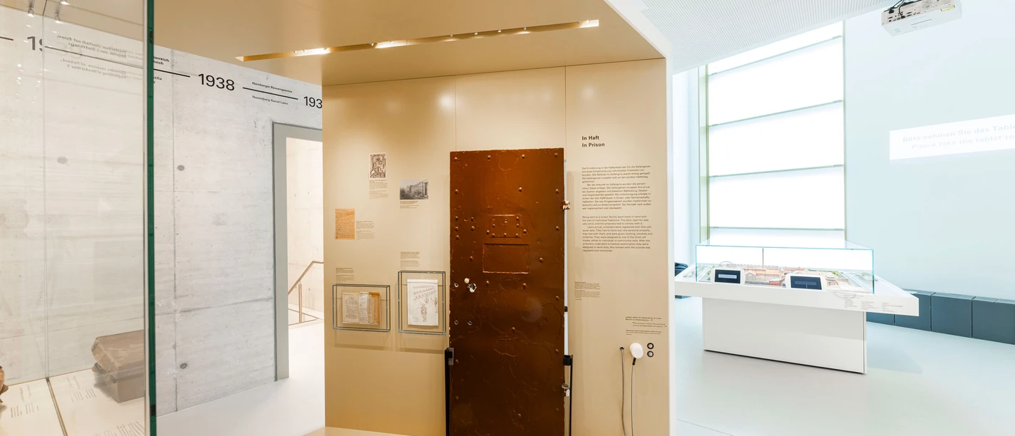 Heller Ausstellungsraum, im Zentrum eine braune Zellentür
