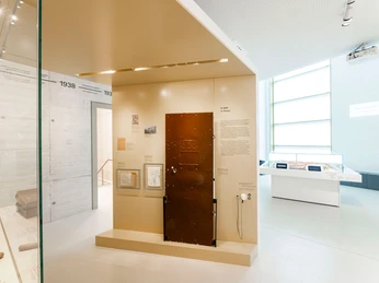 Gedenkstätte-JVA-WF-Ausstellung-Tür.jpg Heller Ausstellungsraum, im Zentrum eine braune ZellentürBright exhibition room, a brown cell door in the centerLyst udstillingsrum, en brun celledør i midtenLichte tentoonstellingsruimte, een bruine celdeur in het midden