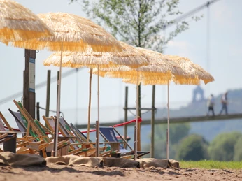 Das Bild zeigt den Mindener Weserstrand mit Strandliege und Sonnenschirm.