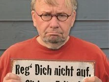 Ein älterer Mann mit ernstem Gesicht hält ein Schild mit der Aufschrift: "Reg' Dich nicht auf. Gibt nur Falten!".