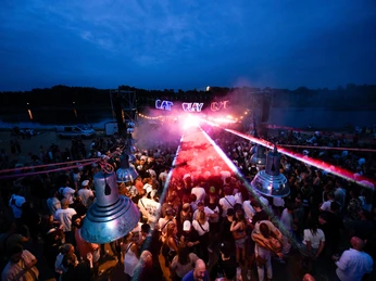 EAT PLAY LOVE Festival The picture shows an evening festival atmosphere with a large crowd in front of an illuminated stage. Lights and fog create an exciting atmosphere, while the letters "EAT PLAY LOVE" shine in bright colors.