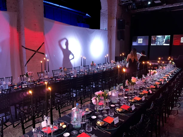 20190730_193806.jpg Lange Tafel mit festlich gedeckten Tischen in einem stimmungsvoll ausgeleuchteten Veranstaltungsraum.