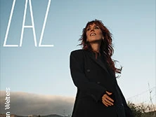 Die französische Sängerin ZAZ steht vor einem klaren Himmel in eleganter schwarzer Kleidung, mit Bergen im Hintergrund.