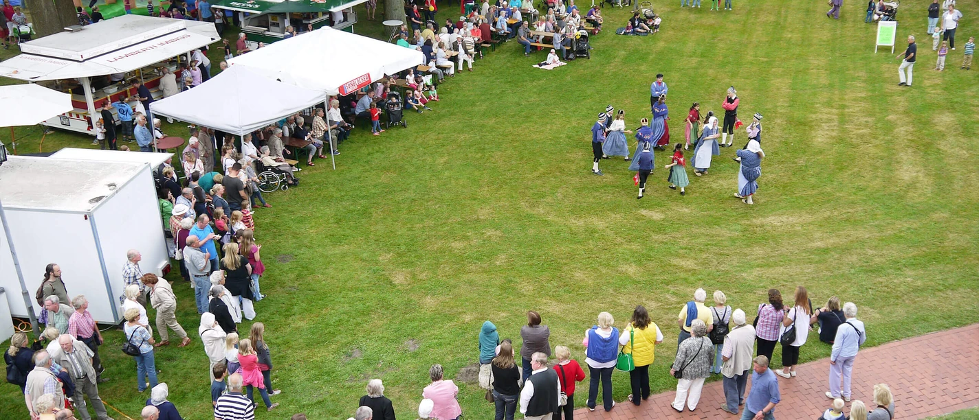 Tag-der-Heimat-von-oben-1.jpg A lively gathering of people of different ages enjoys an open-air festival.