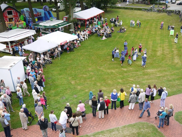 Tag-der-Heimat-von-oben-1.jpg Eine lebhafte Versammlung von Menschen unterschiedlichen Alters genießt ein Freiluftfest.