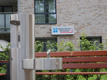 TrinkwasserspenderHwEichenhof 006.JPG Trinkbrunnen aus Edelstahl vor einer modernen Wohnanlage mit dem Schild "Wohngemeinschaft Eichenhof".