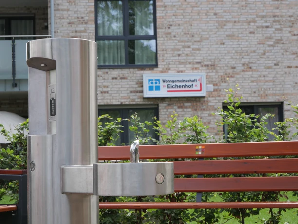 TrinkwasserspenderHwEichenhof 006.JPG Trinkbrunnen aus Edelstahl vor einer modernen Wohnanlage mit dem Schild "Wohngemeinschaft Eichenhof".