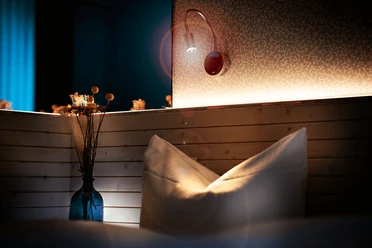 Zimmer im Gästehaus FETTE HENNE in Erkrath Kissen und Lampe in einem stilvoll beleuchteten Gästezimmer mit Holzelementen, dezente Wandtapete.