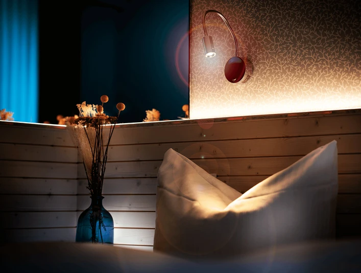 Zimmer im Gästehaus FETTE HENNE in Erkrath Kissen und Lampe in einem stilvoll beleuchteten Gästezimmer mit Holzelementen, dezente Wandtapete.