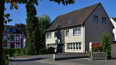Aussenansicht, Hotel Wiedenhof in Hilden Hotel Wiedenhof in Hilden, zweistöckiges Gebäude mit grauer Fassade und begrüntem Vorplatz.