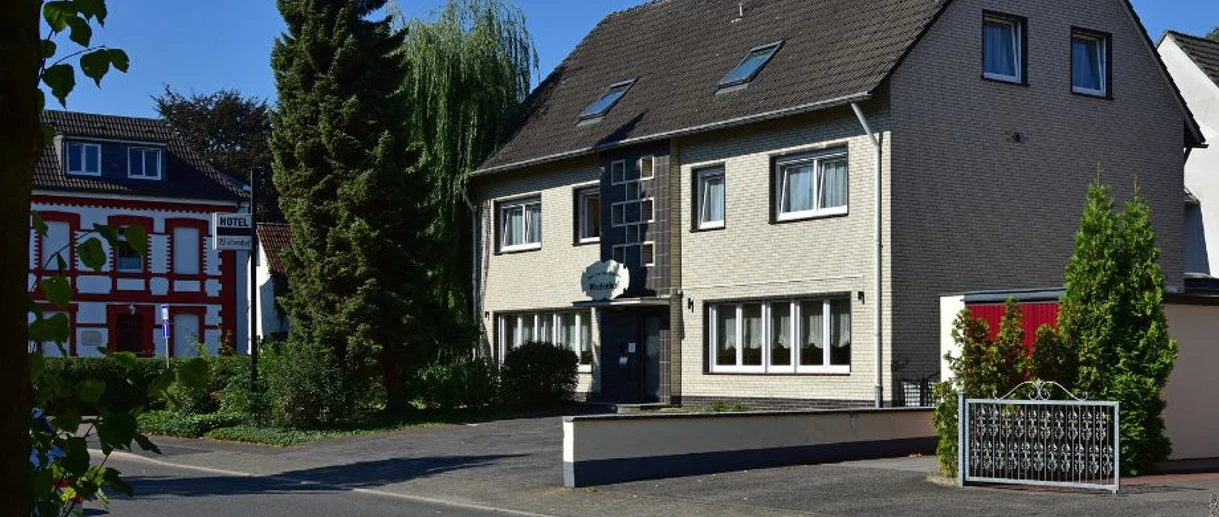 Aussenansicht, Hotel Wiedenhof in Hilden Hotel Wiedenhof in Hilden, zweistöckiges Gebäude mit grauer Fassade und begrüntem Vorplatz.