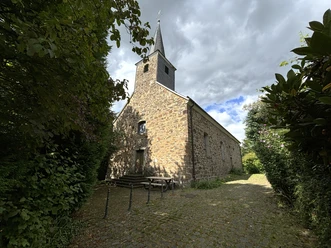 Kirche Johannisberg Alte, malerische Kirche mit gemauertem Turm in sommerlicher Landschaft, umgeben von Bäumen.