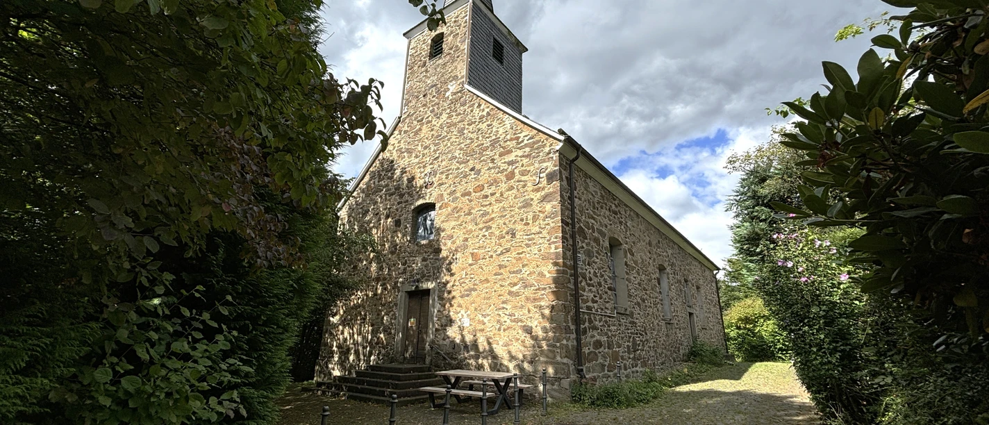 Kirche Johannisberg Alte, malerische Kirche mit gemauertem Turm in sommerlicher Landschaft, umgeben von Bäumen.