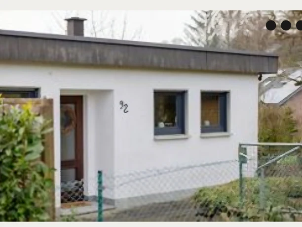 Ferienhaus "Boomen" Ein einstöckiges weißes Haus mit Flachdach und brauner Eingangstür, umgeben von grünem Garten.