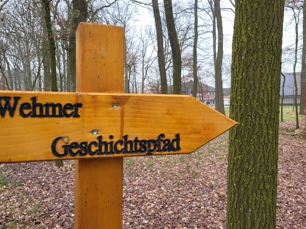 Wehmer Geschichtspfad ©Naturpark Hümmling (37).jpg Holzschild mit der Aufschrift Wehmer Geschichtspfad auf einem Waldweg im Naturpark Hümmling.