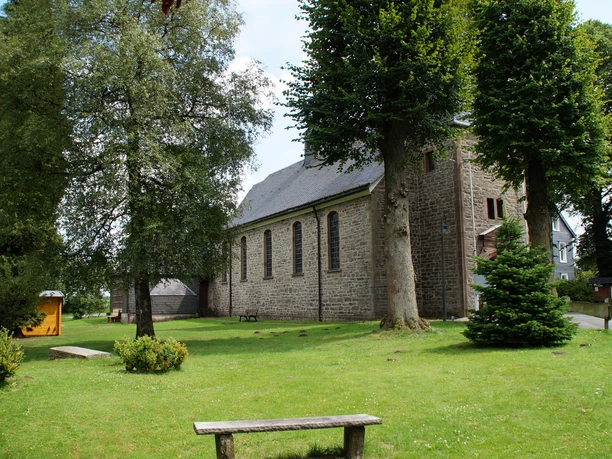 Kirche Wipperfürth-Egen Steinige Kirche inmitten grüner Bäume, mit Parkbank in gepflegtem Rasen; ländliche, ruhige Atmosphäre.