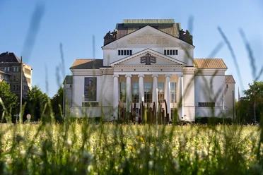 DSC08548.jpg Panoramablick auf ein klassizistisches Gebäude mit Säulenfront und Dreiecksgiebel, umrahmt von einem blühenden Blumenfeld im Vordergrund.