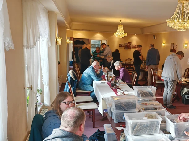 Treffen von Papiergeldsammlern in einem hellen Raum mit Tischen voller Sammlerstücke.