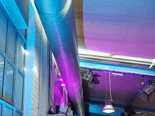 Freies Werkstatt Theater Metallrohr entlang der Decke eines modernen Foyers mit bunten Lichtern und Industriedesign.Metal pipe along the ceiling of a modern foyer with colorful lights and industrial design.