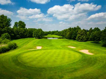 Grüner Golfplatz mit gepflegtem Rasen, umgeben von Bäumen und einem kleinen Teich im Hintergrund.