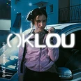 Die Fotografie präsentiert eine Person vor einem Auto mit leuchtendem OKLOU-Schriftzug im Vordergrund.