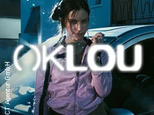 Die Fotografie präsentiert eine Person vor einem Auto mit leuchtendem OKLOU-Schriftzug im Vordergrund.