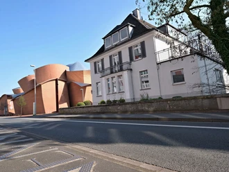 Straßenansicht eines zweistöckigen Hauses mit Schieferdach, daneben ein modernes Backsteingebäude.