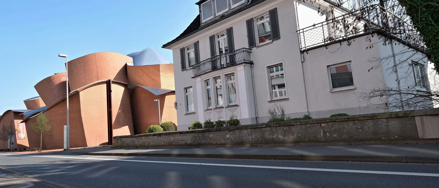 Straßenansicht eines zweistöckigen Hauses mit Schieferdach, daneben ein modernes Backsteingebäude.