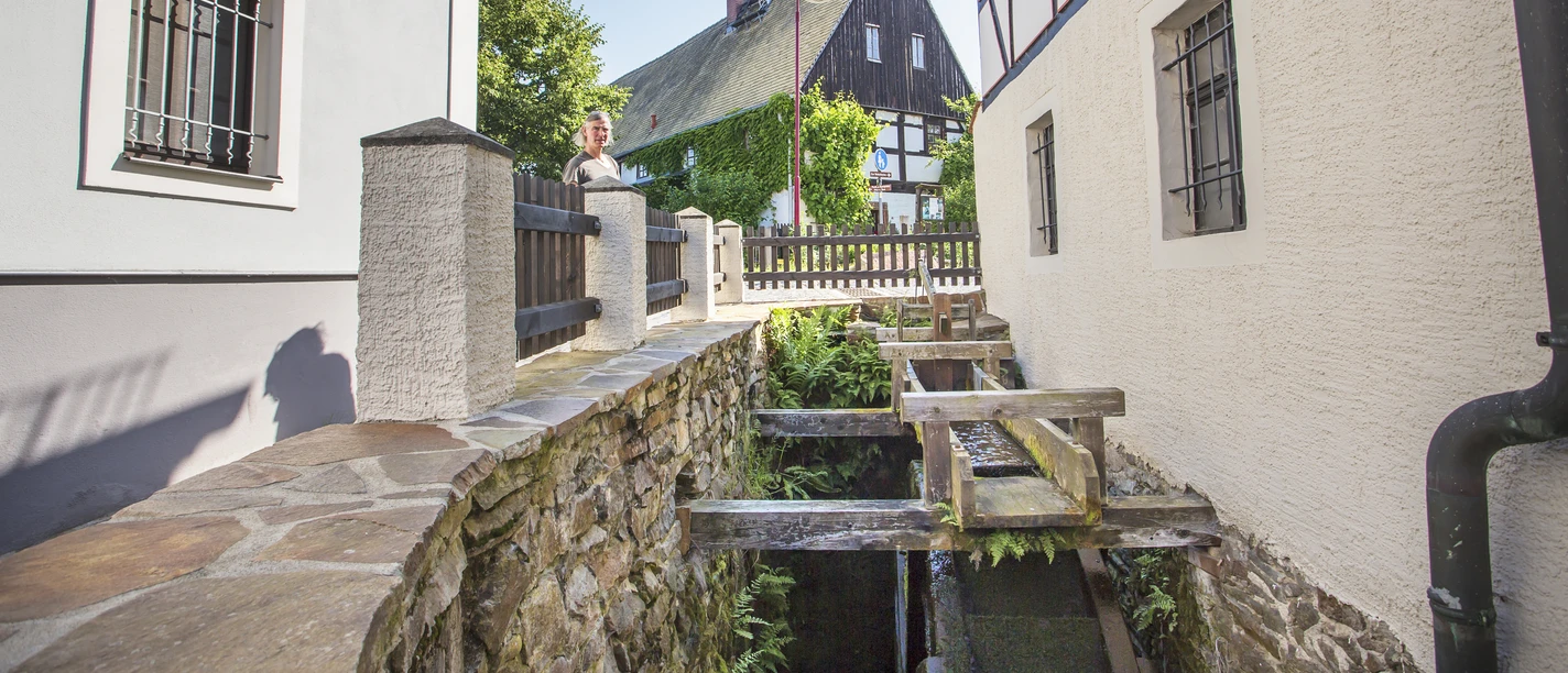La photo montre le moulin à eau du village de Höfgen, encadré par des maisons à colombages et l'auberge historique.