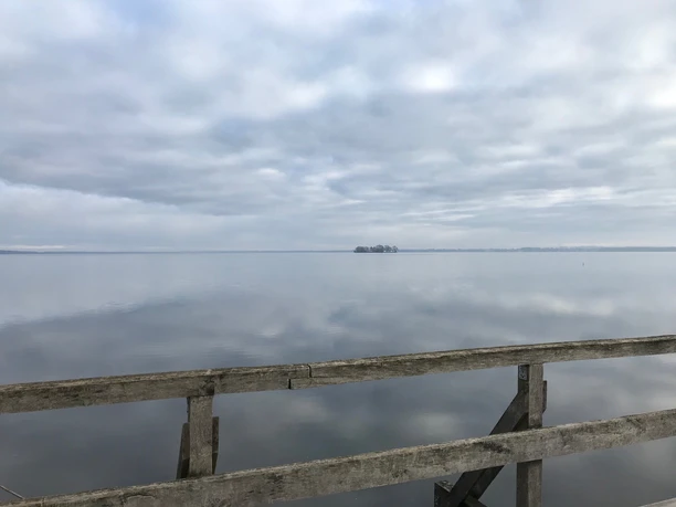 Vogelbeobachtungsturm Winzlar am Steinhuder Meer Holzgeländer vor stiller Gewässerlandschaft mit bewölktem Himmel, im Hintergrund eine kleine Insel.