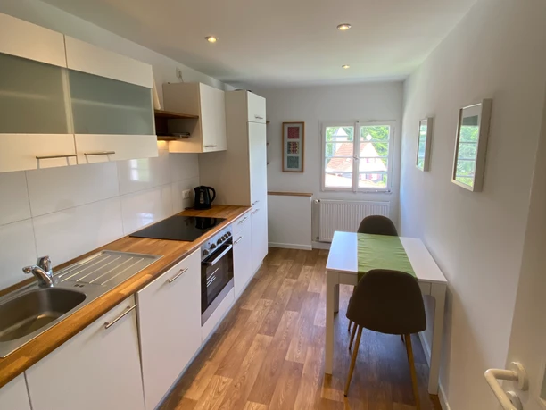 Küche in der Ferienwohnung Privatunterkunft Wolff Helle, moderne Küche mit Holzboden, Esstisch am Fenster, weißen Fronten und zeitgemäßer Ausstattung.