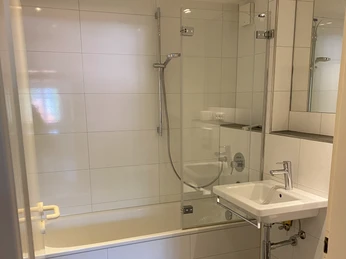 Badezimmer in der Ferienwohnung Privatunterkunft Wolff Helles Badezimmer mit barrierefreier Dusche, Badewanne, Waschbecken und Haltegriff für besseren Halt.