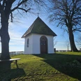 Die Kluskapelle mit zwei Bäumen und Sitzgelegenheiten in Pömbsen.