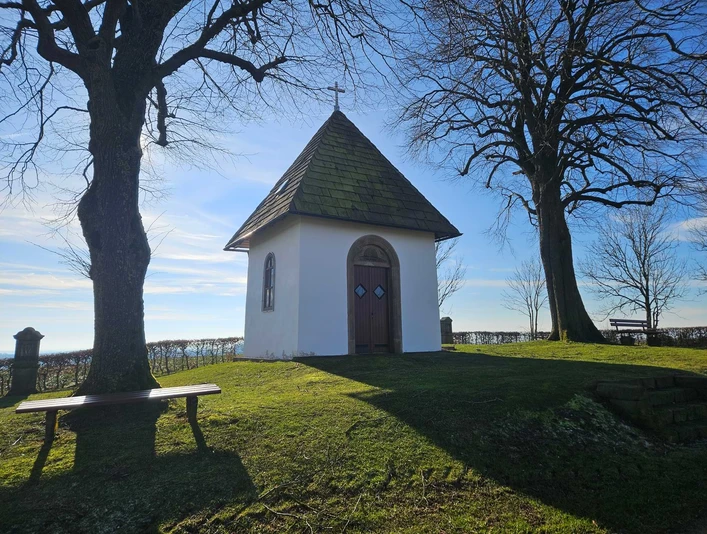 Die Kluskapelle mit zwei Bäumen und Sitzgelegenheiten in Pömbsen.