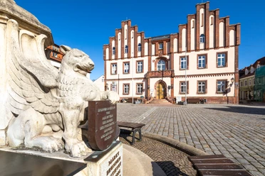 Zdjęcie przedstawia rynek w Mügeln z fontanną i historycznymi posągami, a także rynek miasta.