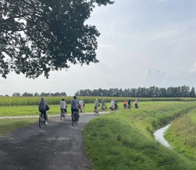 Geführte Radtour durch die Gemeinde Geeste.jpg Gruppe von Radfahrerinnen und Radfahrern auf einer Landstraße zwischen Feldern bei sonnigem Wetter