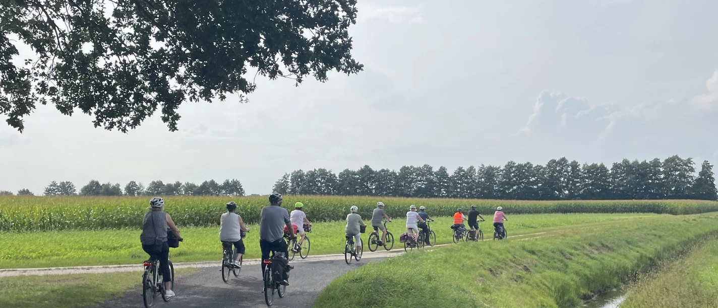 Geführte Radtour durch die Gemeinde Geeste.jpg Gruppe von Radfahrerinnen und Radfahrern auf einer Landstraße zwischen Feldern bei sonnigem Wetter