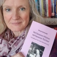 Sonja Schmidt Sonja Schmidt trägt eine Bluse und hält ihr Buch "Verlassene Mütter, verlassene Töchter" vor einem Bücherregal.
