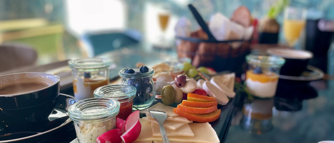 Frühstück_Richhome_@_CCBYSA_Teutoburger Wald_Stadt_Schloß Holte-Stukenbrock.jpg Frühstückstisch mit Kaffee, Käse, Gurken und Aufstrichen, Körbchen mit Brötchen im Hintergrund