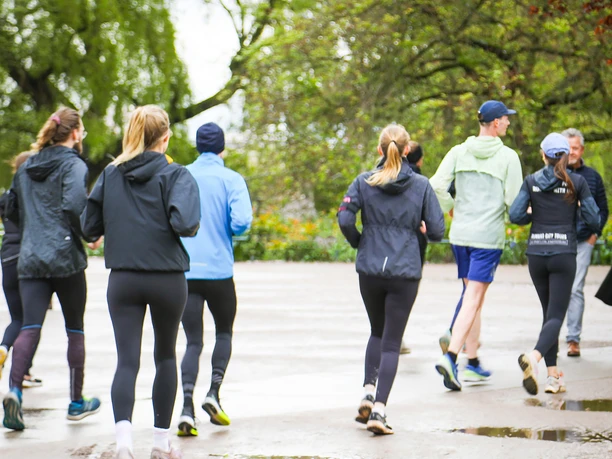 Grupa co najmniej 7 osób uprawiających jogging wzdłuż asfaltowej ścieżki.