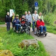 Inklusion Eine Gruppe von acht Personen, davon drei im Rollstuhl, genießt einen Spaziergang auf einem Waldweg.