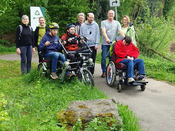 Inklusion Eine Gruppe von acht Personen, davon drei im Rollstuhl, genießt einen Spaziergang auf einem Waldweg.