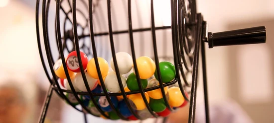 Bingo-Abend Bunte Bingo-Kugeln rotieren in einem metallischen Käfig, während Teilnehmer im Hintergrund gespannt zusehen.