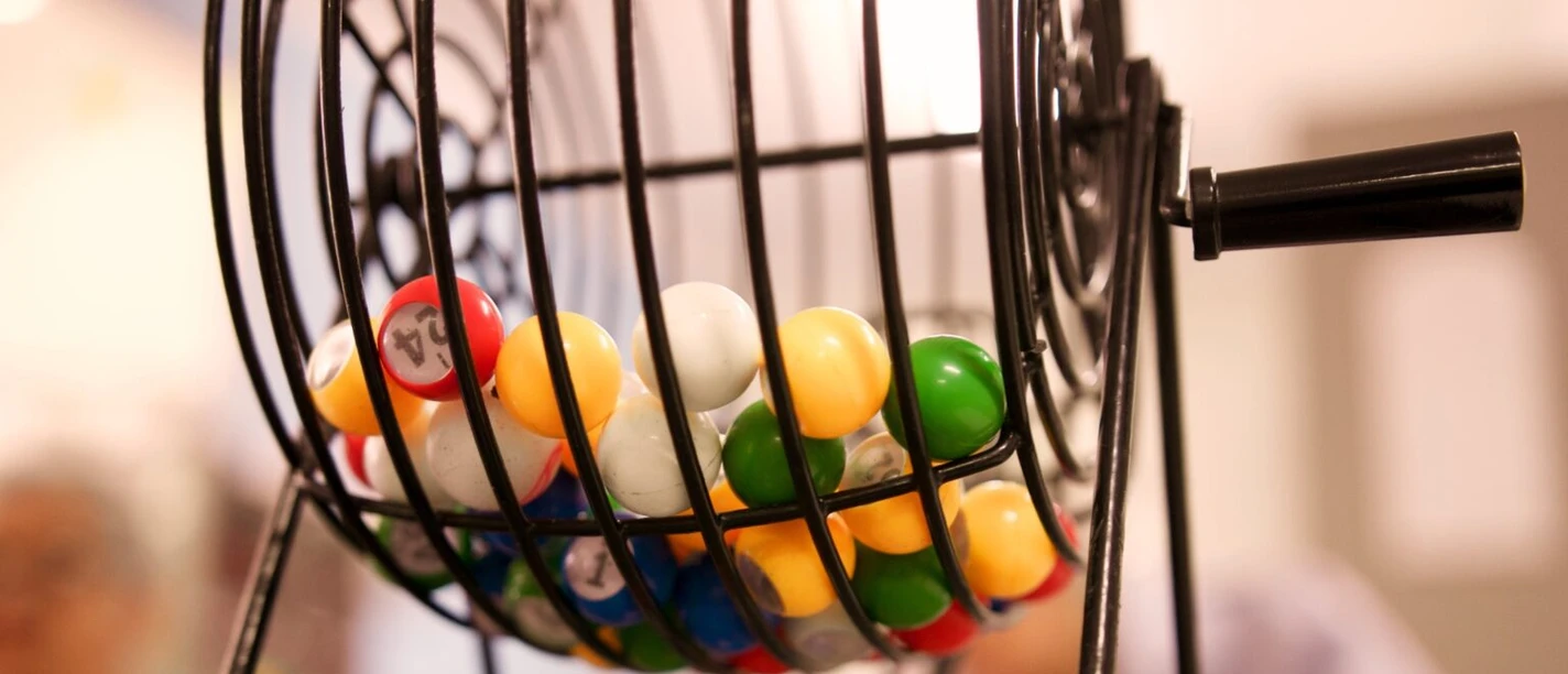 Bingo-Abend Bunte Bingo-Kugeln rotieren in einem metallischen Käfig, während Teilnehmer im Hintergrund gespannt zusehen.