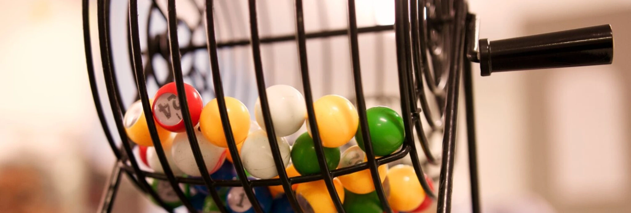 Bingo-Abend Bunte Bingo-Kugeln rotieren in einem metallischen Käfig, während Teilnehmer im Hintergrund gespannt zusehen.