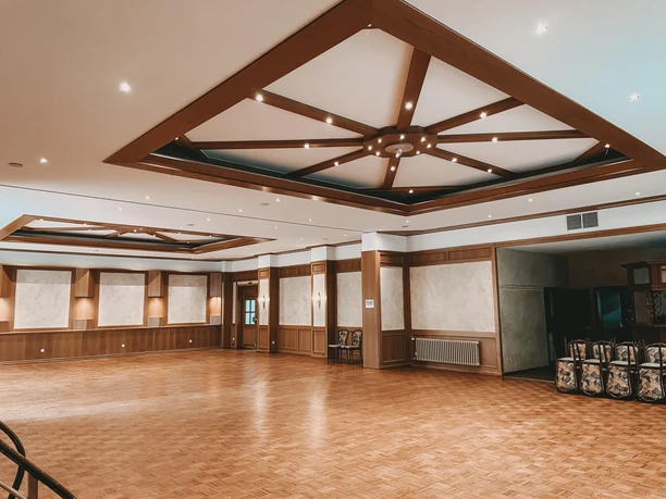Großer, eleganter Veranstaltungsraum mit Parkettboden, Holzbalkendecke und warmem, sanftem Licht.