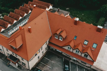 Herford-Gästehaus Janzen-Aussen Luftbild.jpeg Luftbild eines großen Gebäudekomplexes mit rotem Ziegeldach, umgeben von parkenden Autos und Bäumen.
