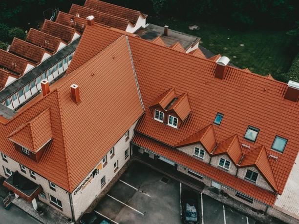Herford-Gästehaus Janzen-Aussen Luftbild.jpeg Luftbild eines großen Gebäudekomplexes mit rotem Ziegeldach, umgeben von parkenden Autos und Bäumen.